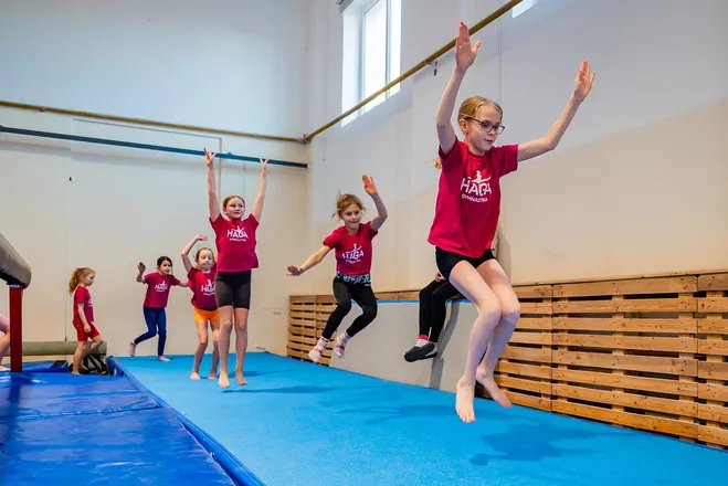 Holky z gymnastického kroužku HAGA skáčou v řadě na žíněnce